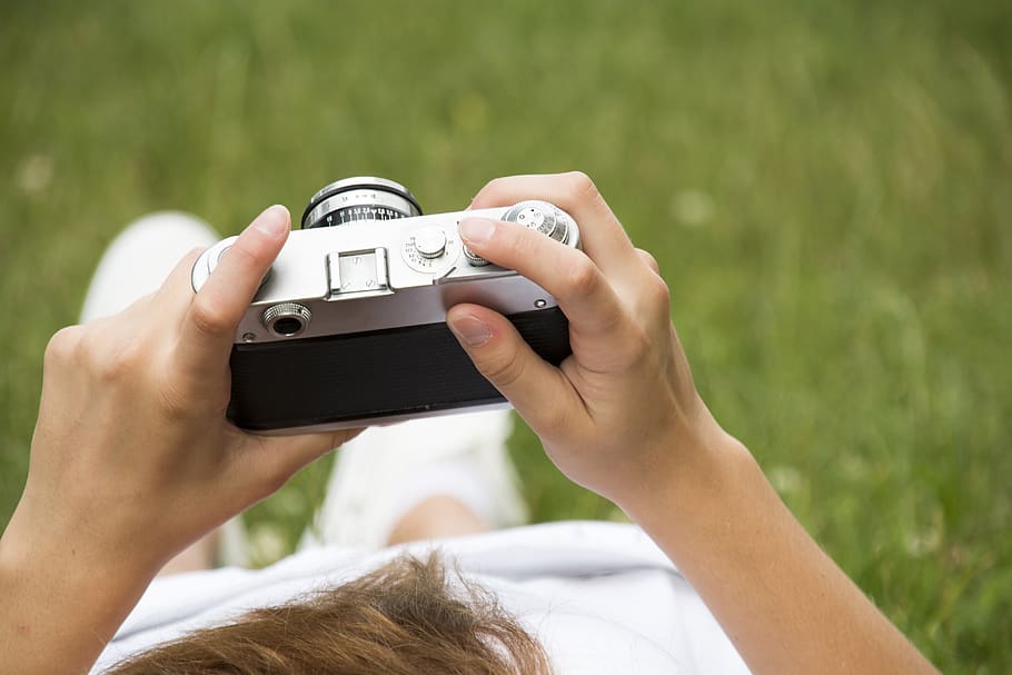 Person in White Dress Holding Grey and Black Camera on Grassland HD wallpaper