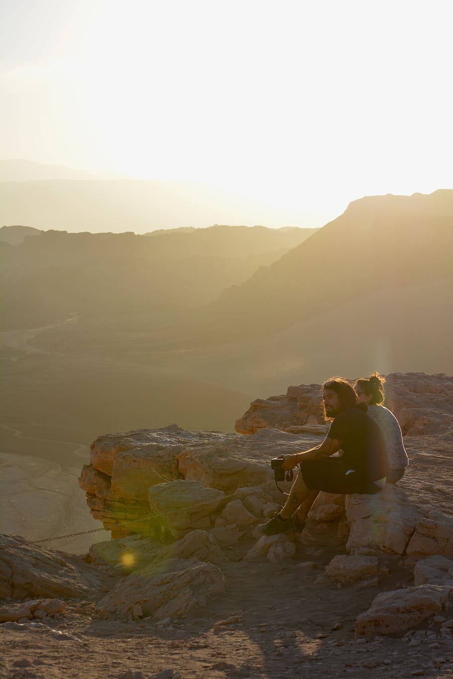 Man Sitting on Stone Beside Woman, camera, clouds, daylight, desert HD wallpaper