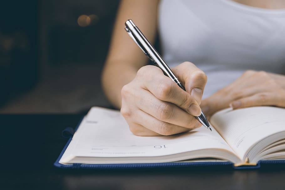The woman’s hand holds a pencil and writes a plan into a diary at home HD wallpaper