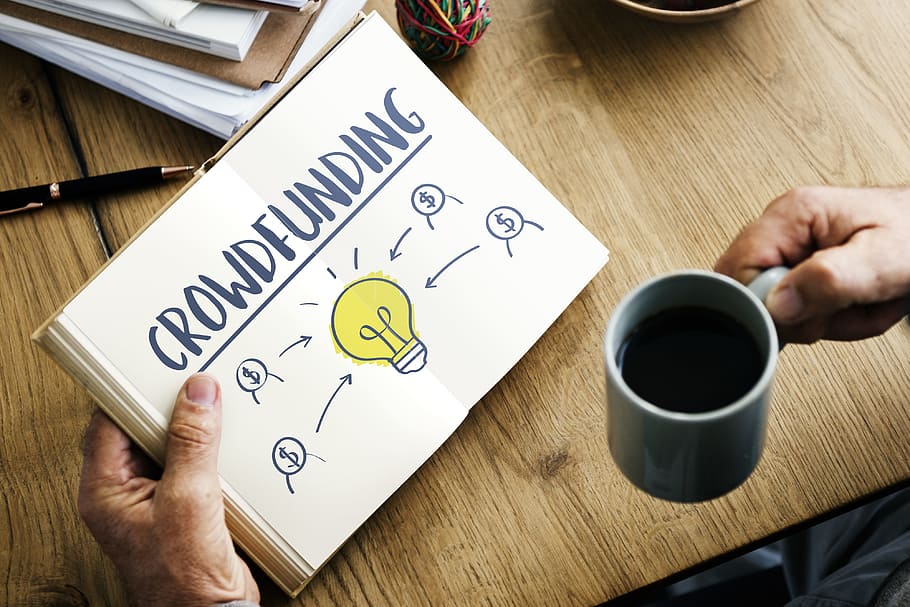 Person Holding Crowdfunding Book and Cup of Coffee, close-up