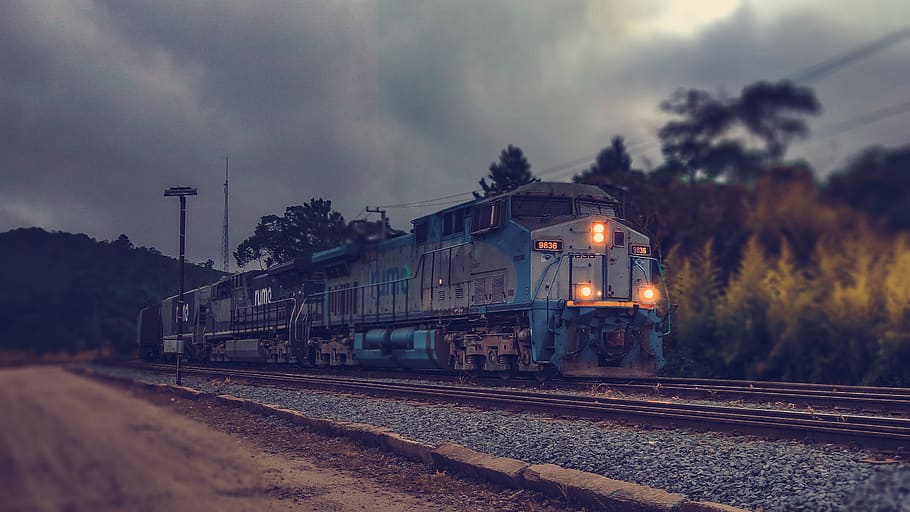 selective focus photography of gray and blue train passing by under cloudy sky