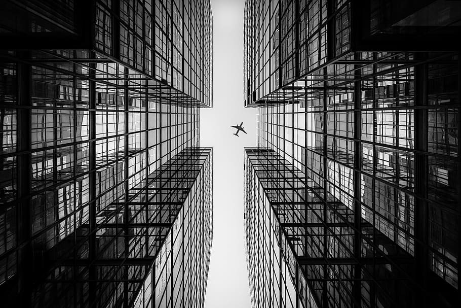 low angle photography of airplane passing above high-rise building