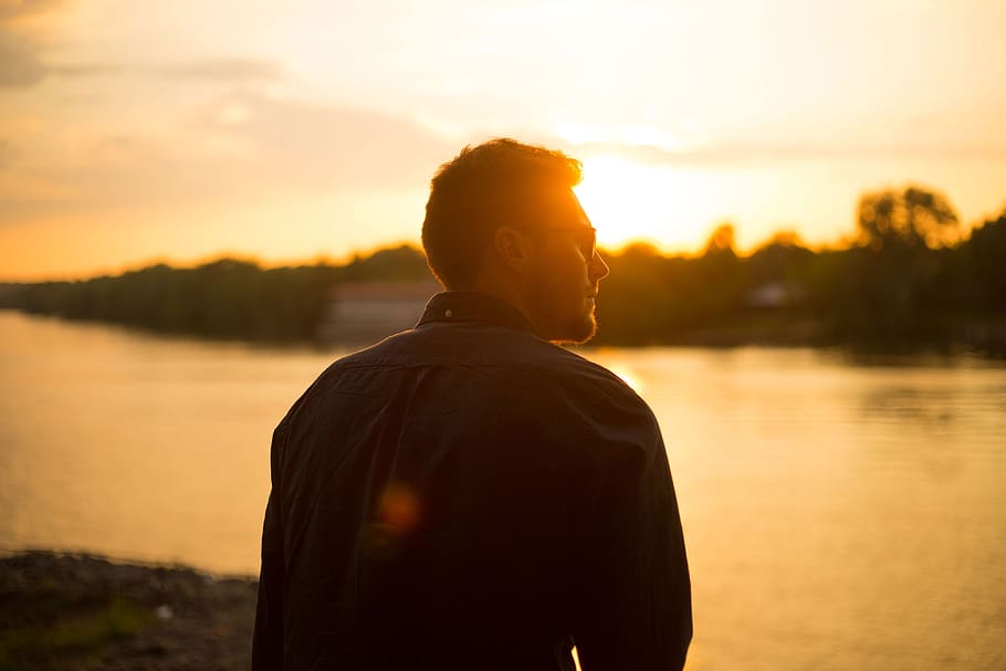 Man Sitting Near Large Body of Water Under Clear Sky during Sunset HD wallpaper