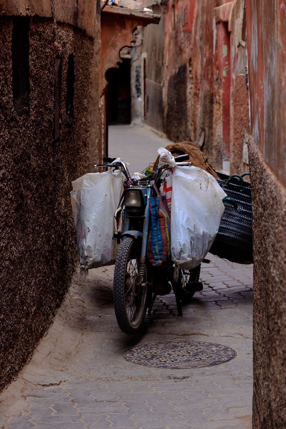 blue motorcycle between brown wall, narrow, backalley, street