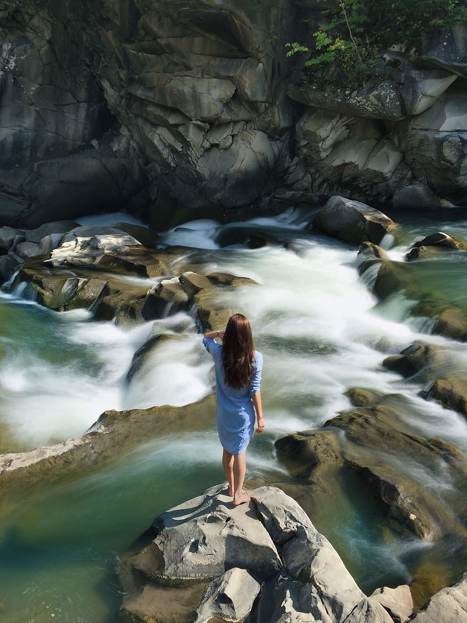 Woman in Blue Long-sleeved Dress Standing in Middle of Rock With Raging Water HD wallpaper