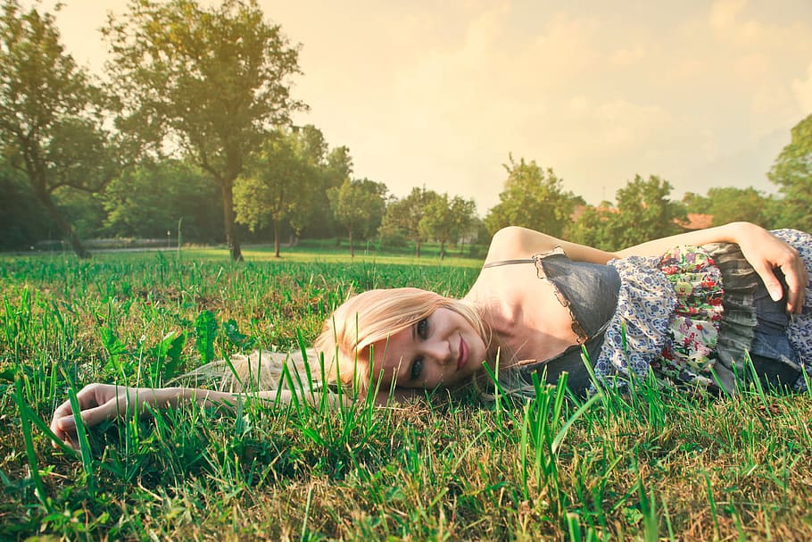 Young Blonde Woman In Spaghetti Straps Floral Skirt Lying On Grass In Sunlight