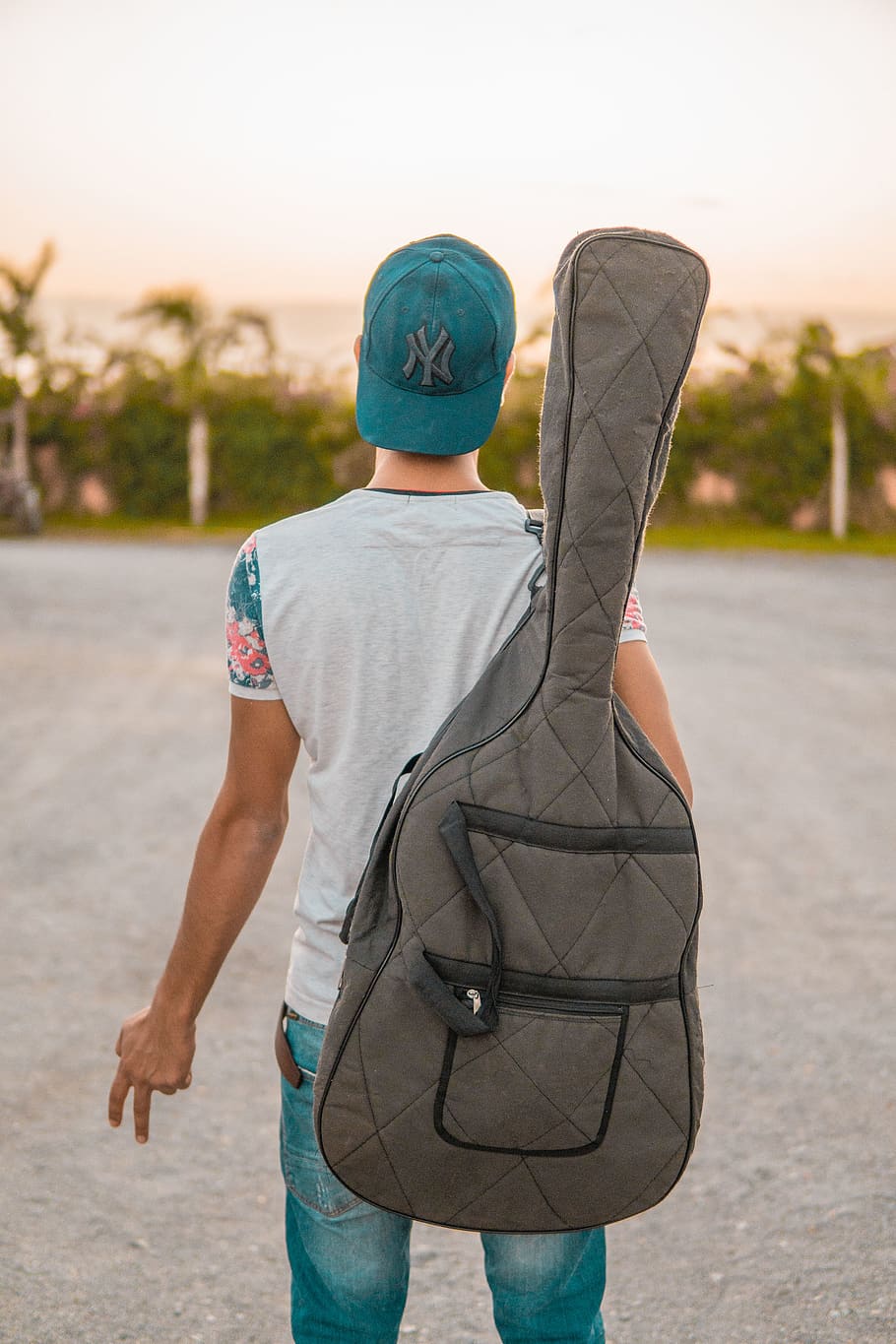 man looking at green trees carrying grey guitar case, person