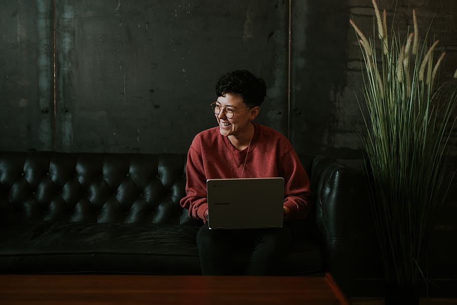 smiling man using laptop computer while sitting on black leather sofa, HD wallpaper