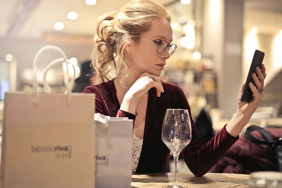 A young blond woman wearing a satin dress looks at her mobile phone while enjoying a glass of wine, HD wallpaper
