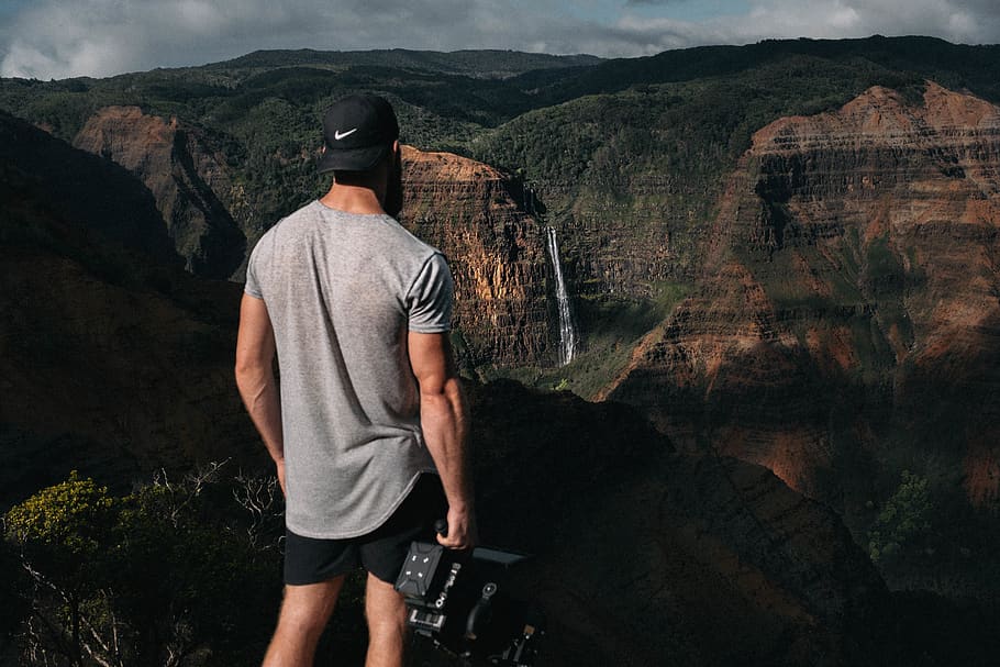 man in gray shirt and black Nike cap standing near canyon, mountain