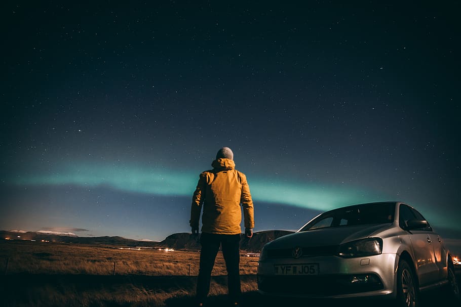man standing beside gray car while watching Aurora Borealis phenomenon