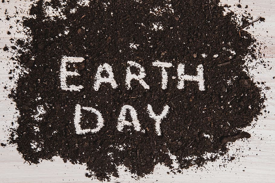 The text EARTH DAY written out in dark soil on a white wooden surface to convey a message to conserve natural resources