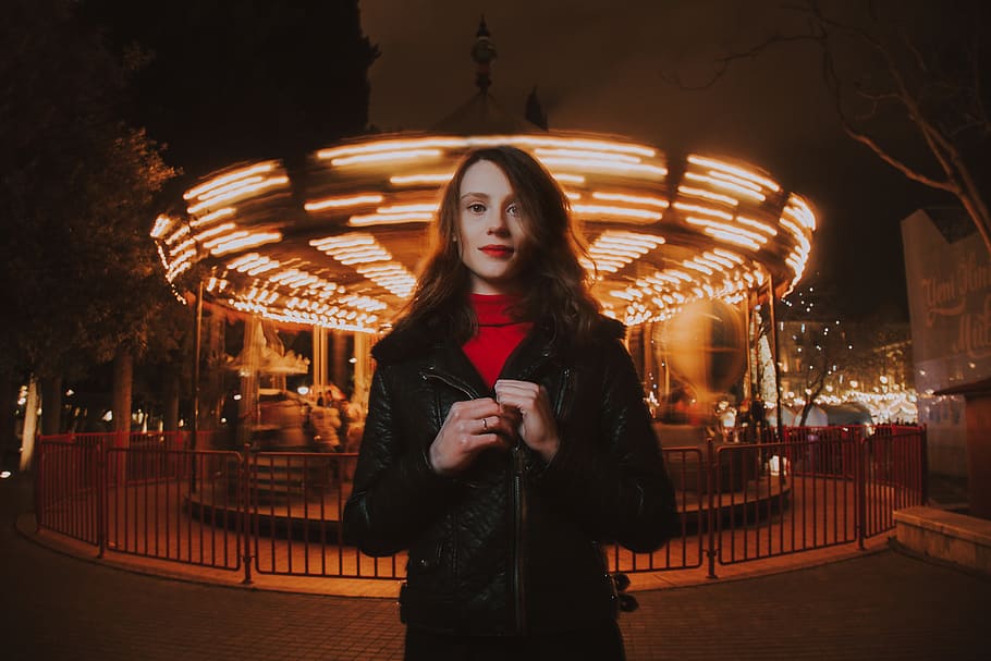 Woman Wearing Black Leather Jacket and Red Turtle-neck Shirt Standing in Front of Carousel Ride HD wallpaper