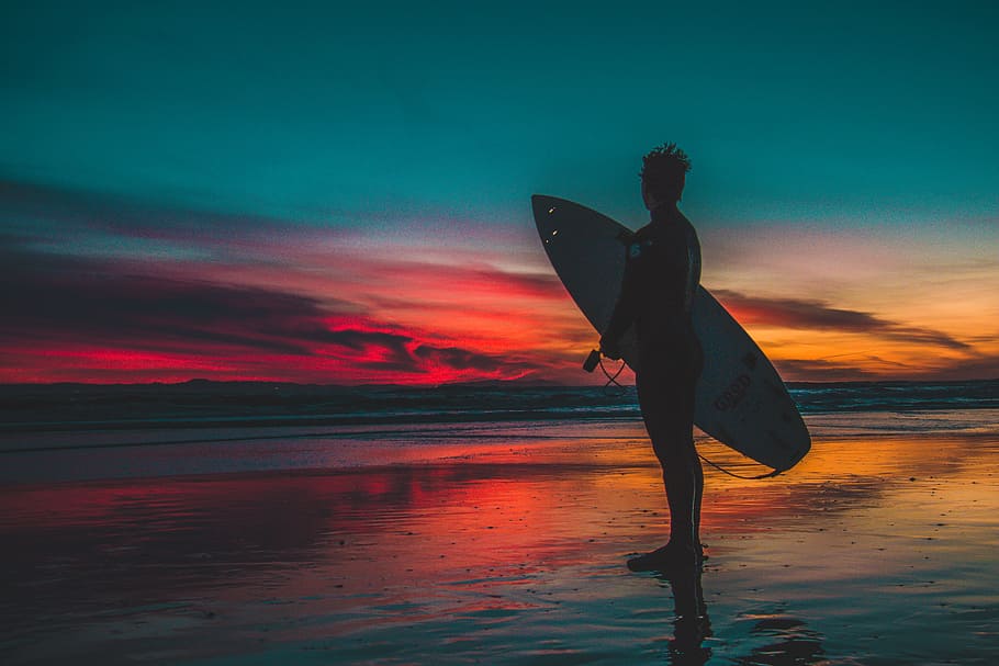 Silhouette of Man in Wet Suit Holding White Surfboard While Standing on Beach during Golden Hour HD wallpaper