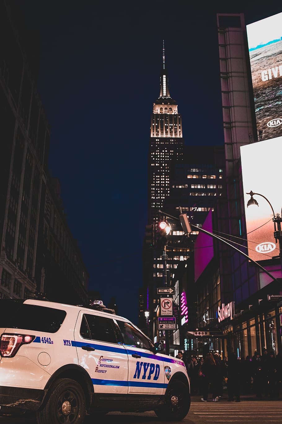white and blue NYPD Ford Explorer police cruiser on road with view of Empire State building during night time