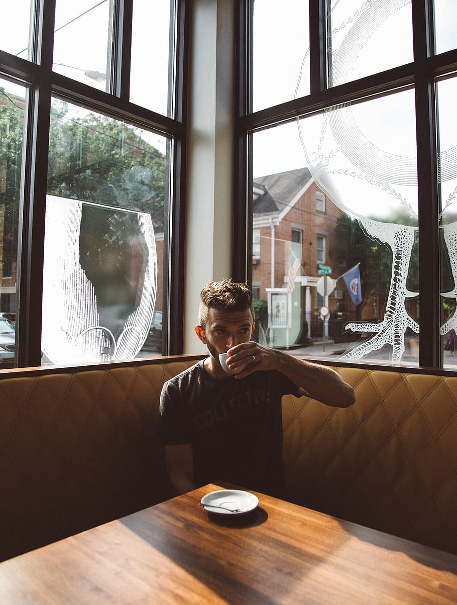 man sitting on brown sofa while drinking, window, one person HD wallpaper
