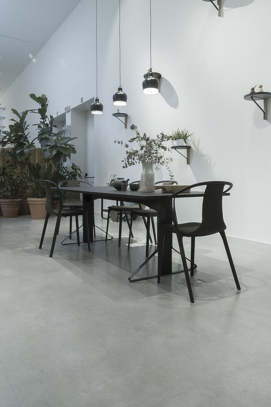 black wooden table and metal chairs near white wall with three pendant lamps above table