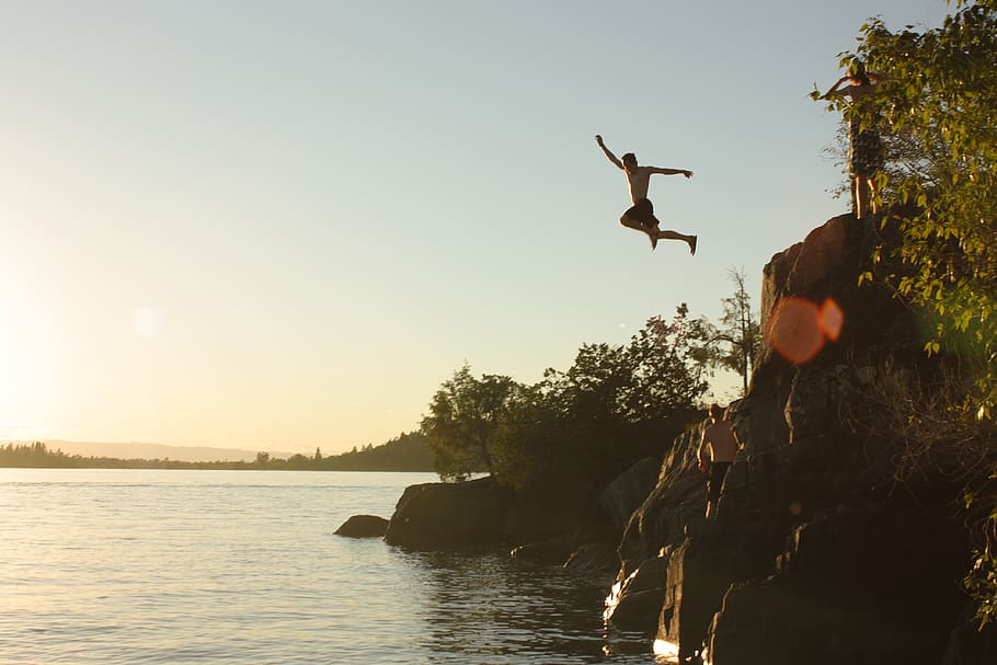 person diving from cliff to body of water during sunset, fun
