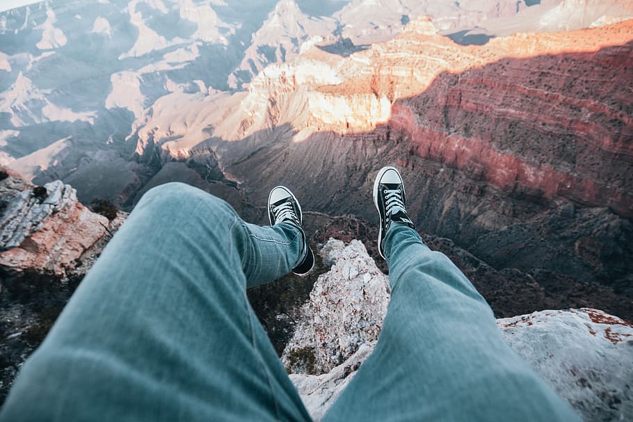 A top view of adventurer s legs dangled over canyon edge, landscape