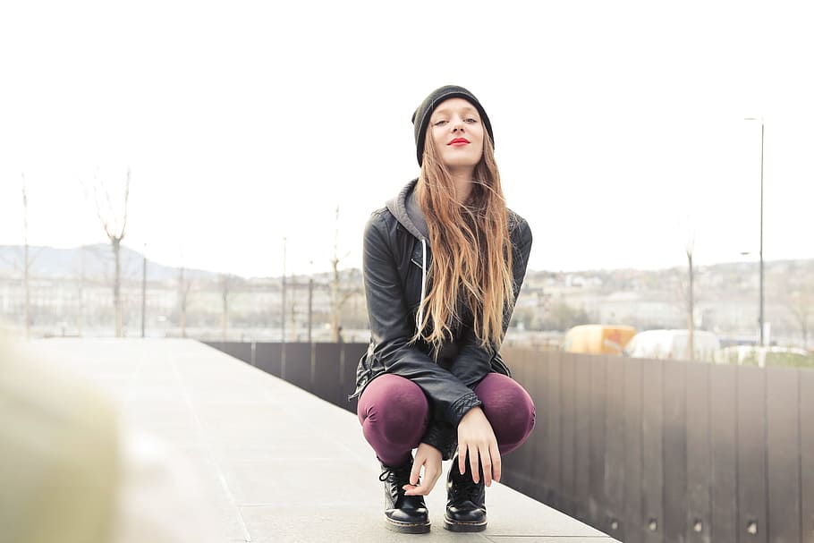 A young blonde woman wearing a black leather jacket and purple red leggings sitting on her toes in squatting posture, HD wallpaper