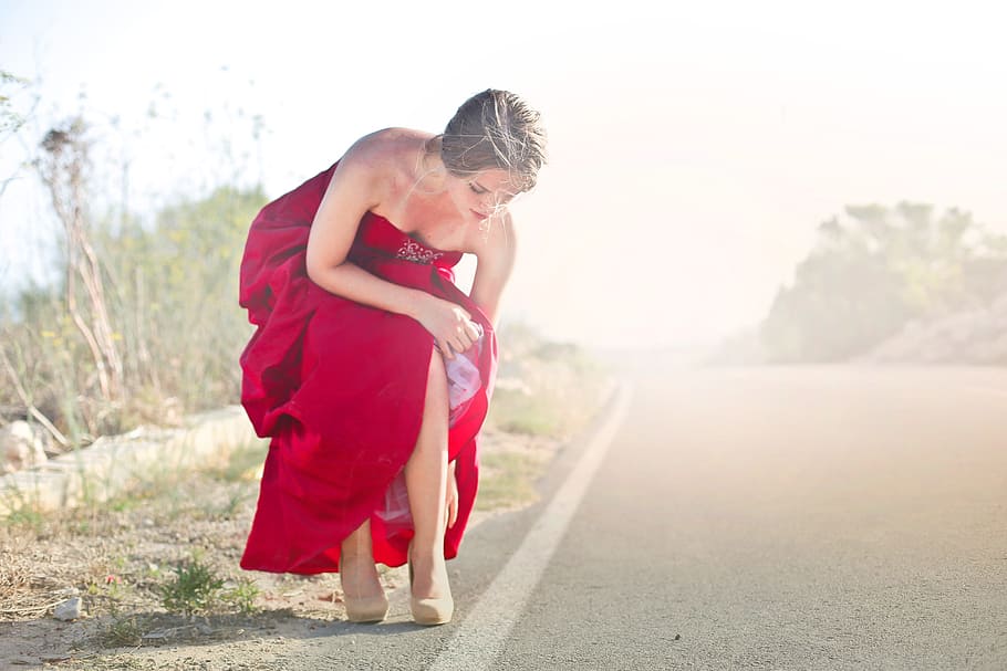 Young Adult Woman In Red Party Gown Dress Adjusting Her Shoes During Photo Shoot