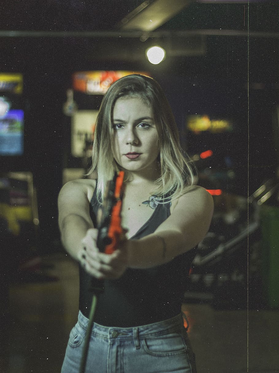 Photo of Standing Woman Holding Gun Game Controller at an Arcade