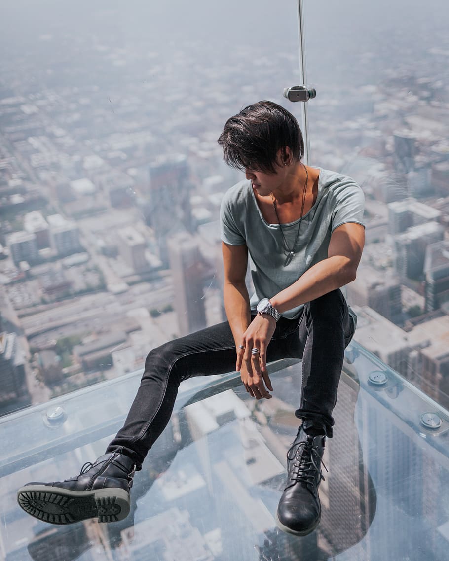 man sitting on top of clear glass roof top, clothing, footwear