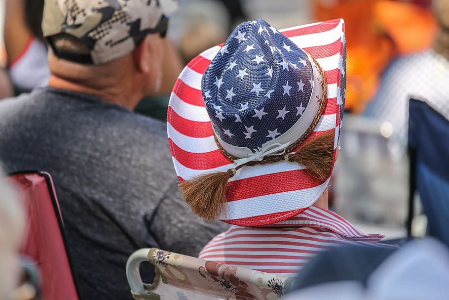 Woman watching a parade wearing a hat painted with American Flag pattern.
