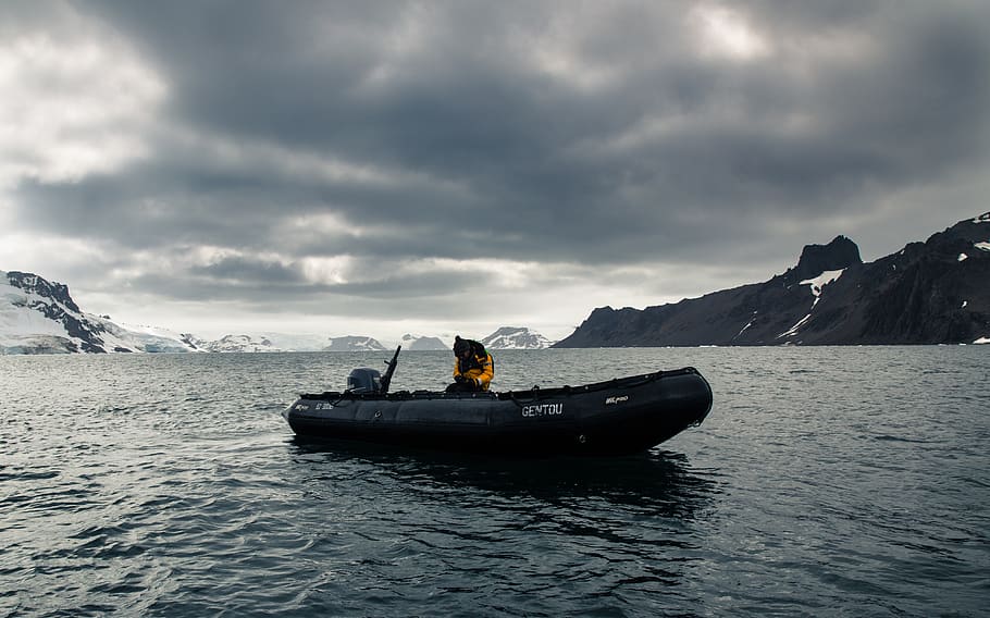 Man in Motor Boat in Front of Snow-covered Mountain Under Gray Cloudy Sky HD wallpaper
