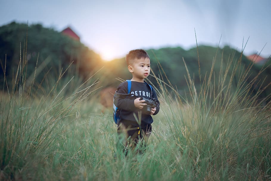 Shallow Focus Photography of Boy Standing on Green Grass Holding Camera HD wallpaper