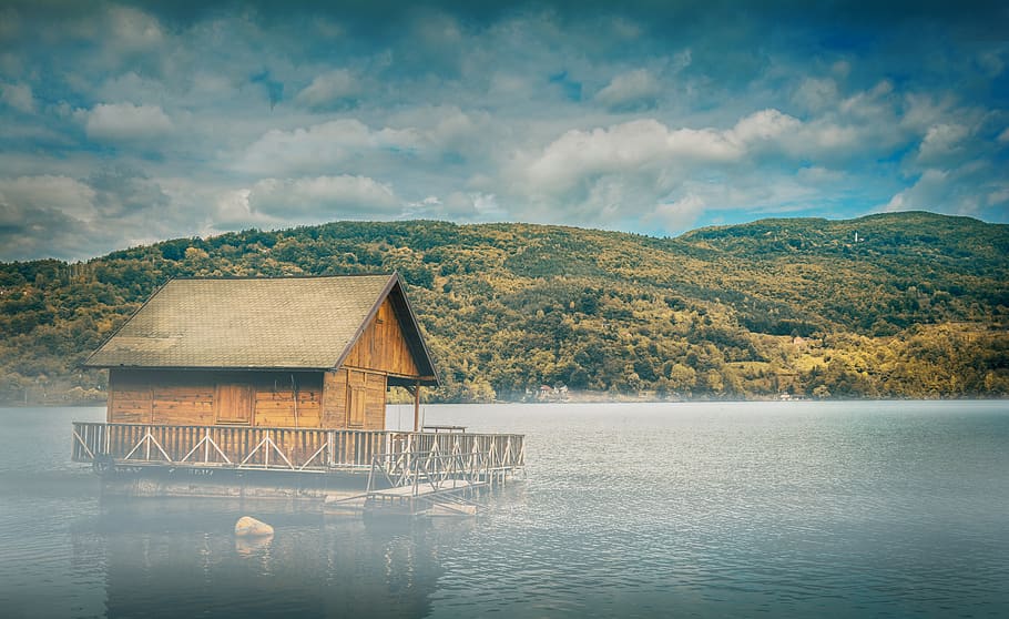 brown wooden floating cottage in middle of body of water with mountain in background