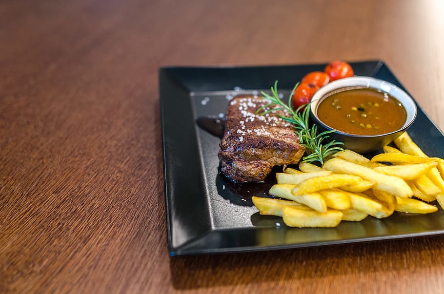 Grilled Beef With Fries and Sauce on Black Ceramic Plate, close-up