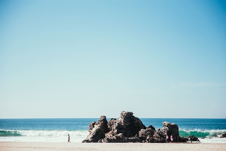 Tourists on a rocky seashore in sunlight with horizon in the background HD wallpaper