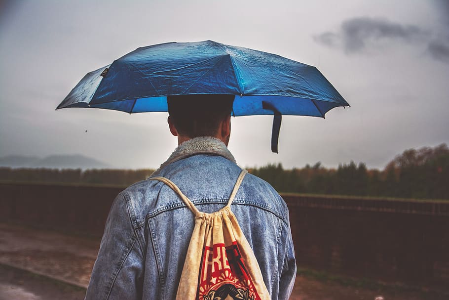man under blue umbrella with brown drawstring bag, protection