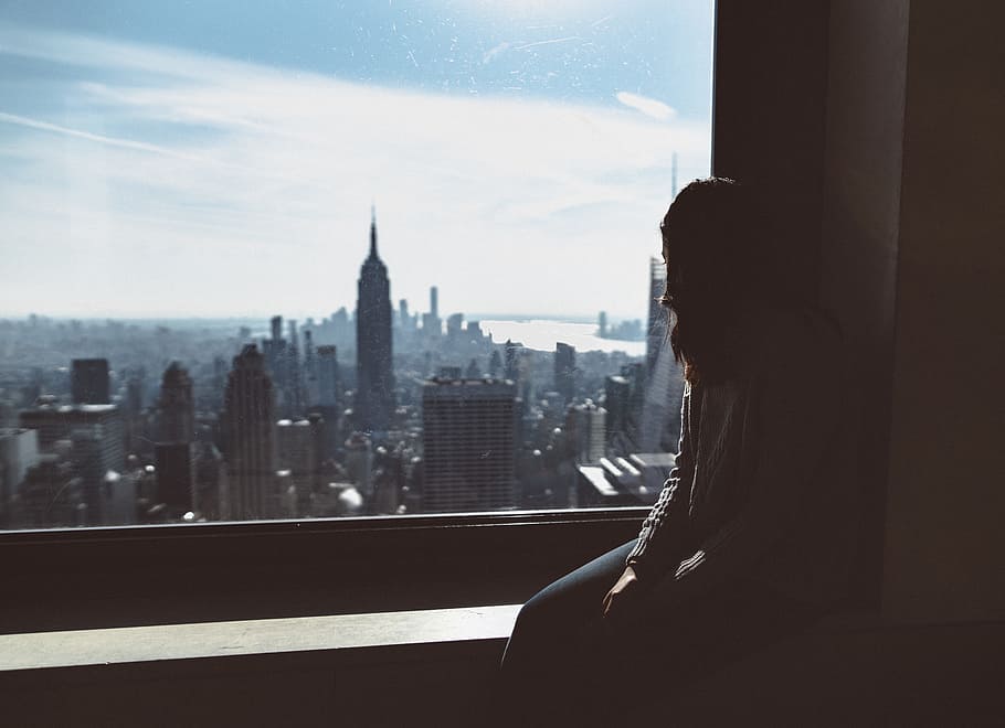 woman sitting on window edge looking at Empire State tower, building