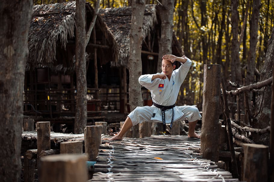 man wearing karate gi squatting on wooden dock, human, person
