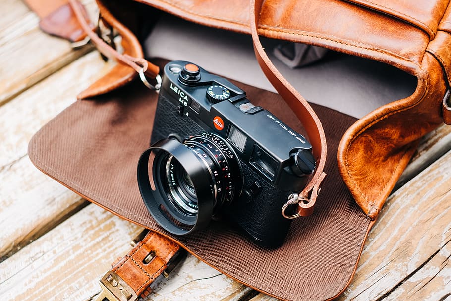 black DSLR camera with brown leather bag on brown surface, lens