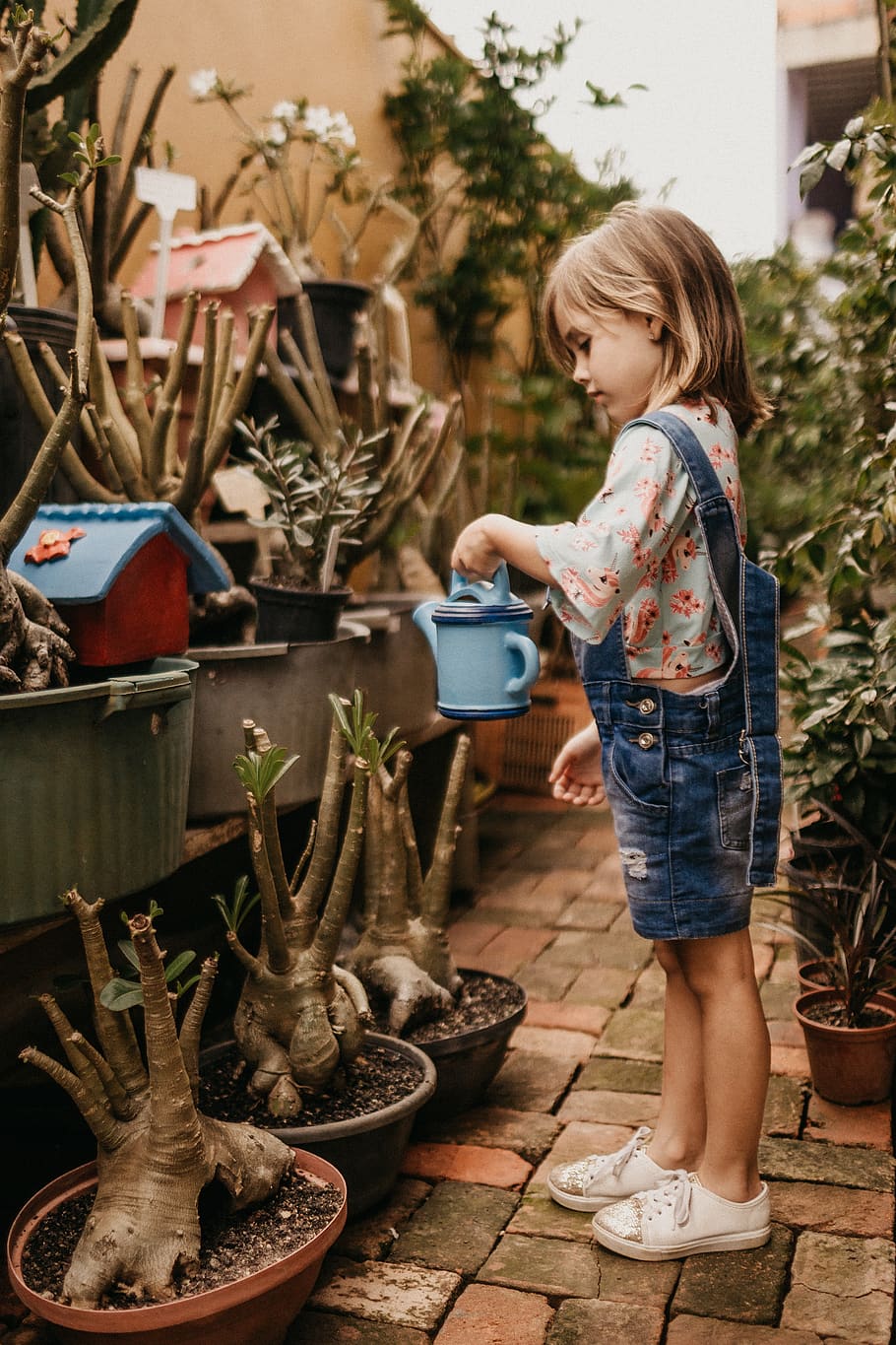 girl wearing blue romper holding teal watering can, footwear