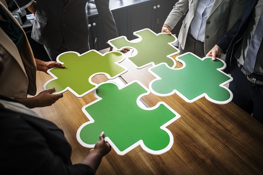 Four People Holding Four Jigsaw Pieces on Top of Brown Wooden Table HD wallpaper