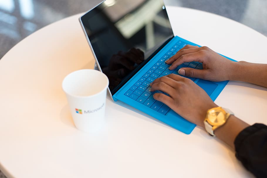 Person Wearing Round Gold-colored Watch Using Black Tablet Computer With Blue Detachable Keyboard on Round White Wooden Table HD wallpaper