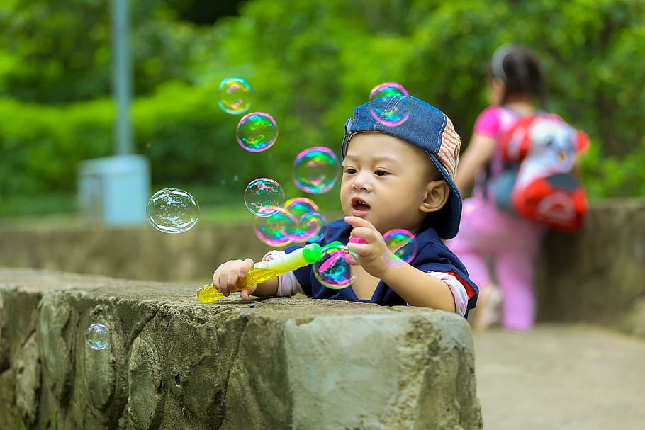 Boy in Blue Fitted Cap Playing Bubbles and Leaning on Grey Concrete Wall at Daytime HD wallpaper
