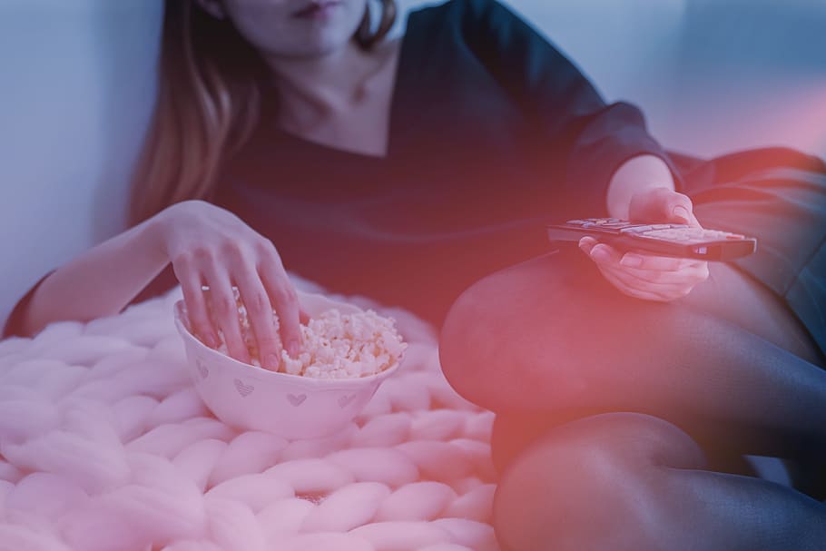 Woman is watching TV and eats a popcorn from bowl, one person