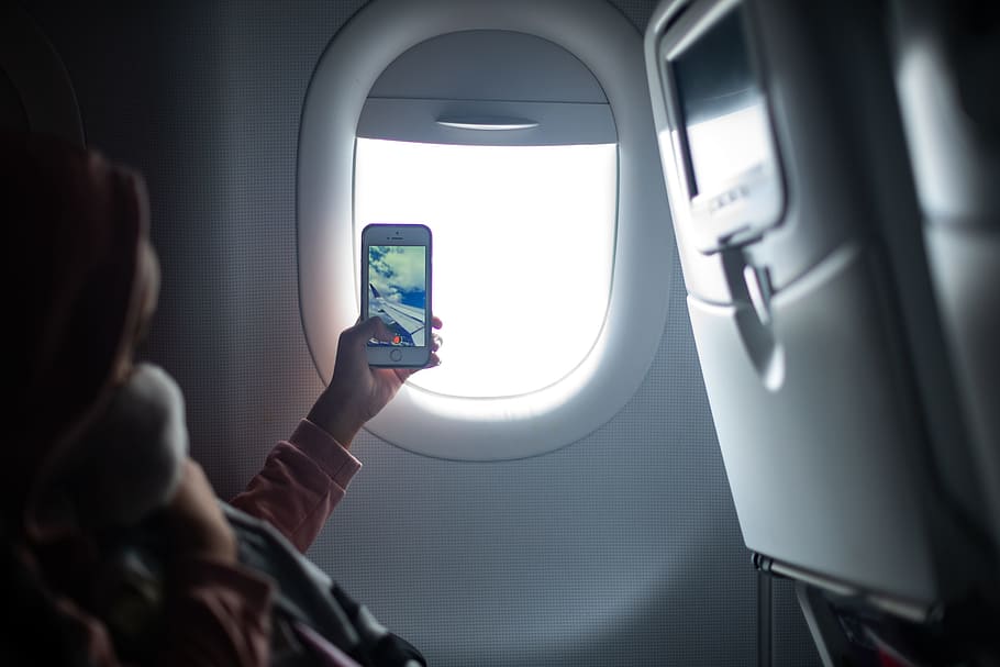 woman holding iPhone taking photo inside airplane, window, hand