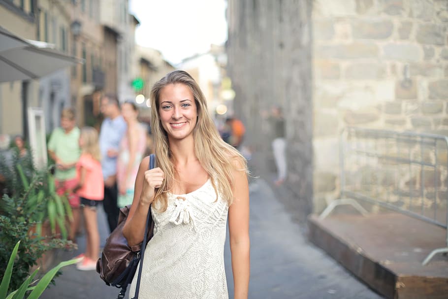 A young blonde woman in white dress carrying a leather bag posing in the street
