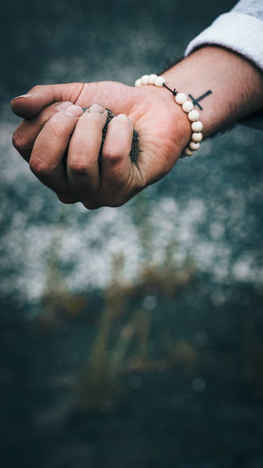 person wearing beaded white bracelet with dirt in hand, human