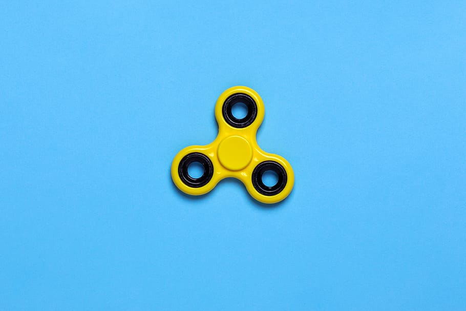 Yellow Tri-spinner Fidget Toy on Blue Tabletop, background, blue background