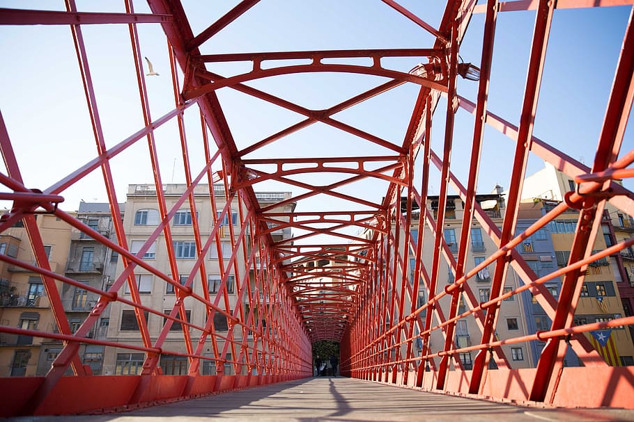 A red caged-design walking bridge with building apartments in the background HD wallpaper