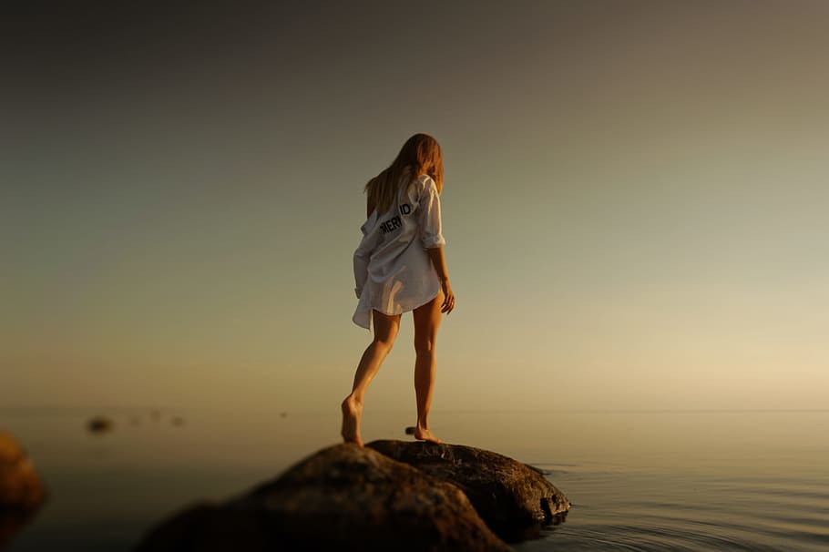woman walking over brown rocks near body of water during daytime HD wallpaper