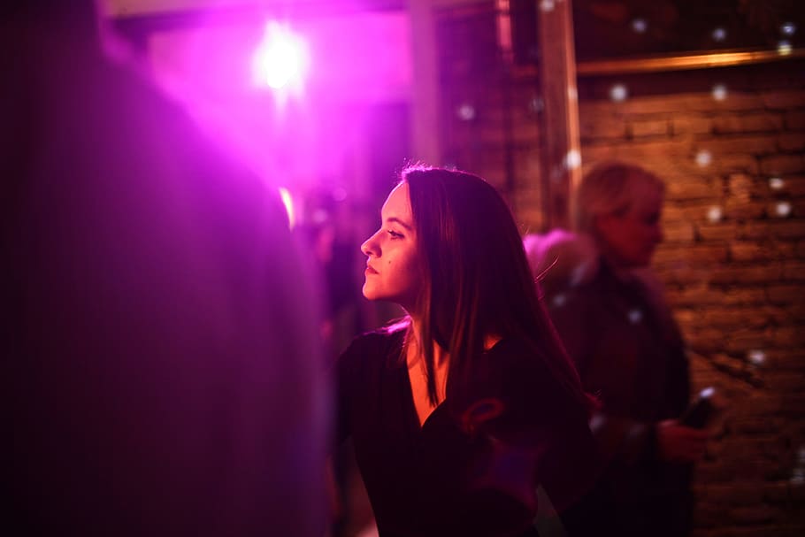 A young brunette in black dress woman sitting in a bar with colourful lights
