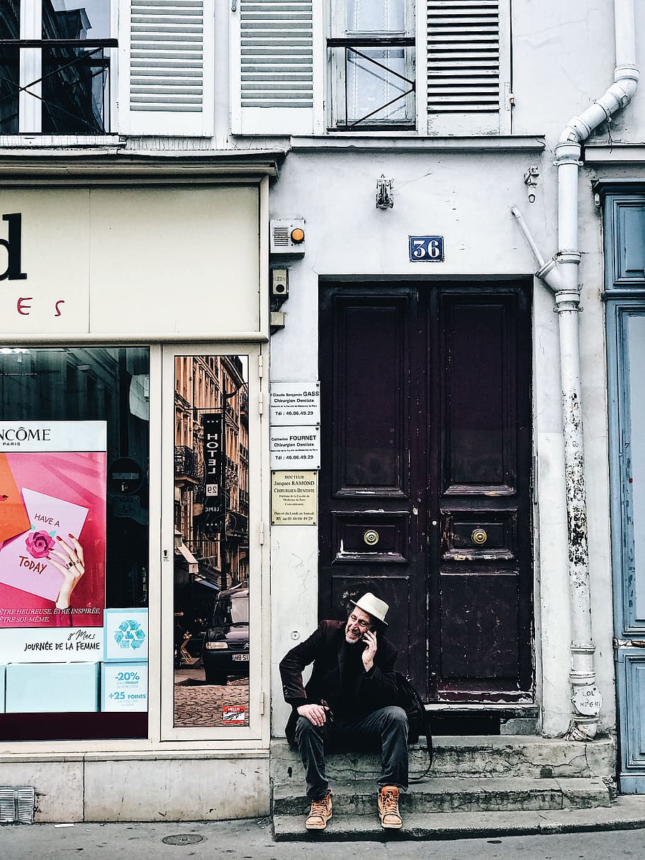 man sitting outside door while calling using smartphone during daytime HD wallpaper